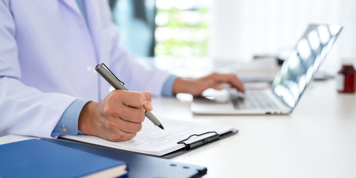 Doctor looking at laptop screen writing in notebook for research planning or medical tech innovation in hospital office. Healthcare medic worker, research strategy book notes and online communication.