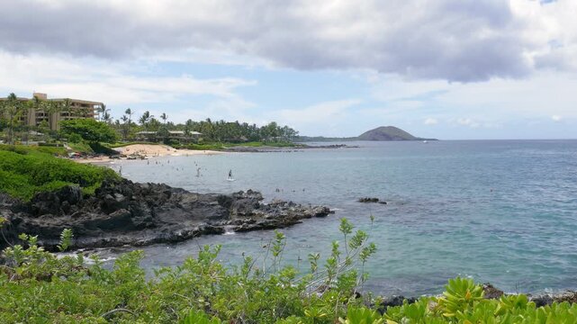 Wailea-Makena coastal area of Maui, Hawaii with a volcanic rock shoreline, tourists on the white sand Polo beach beyond and the Puu Olai Cinder Cone in the distance. Sunny day during April, 2023.