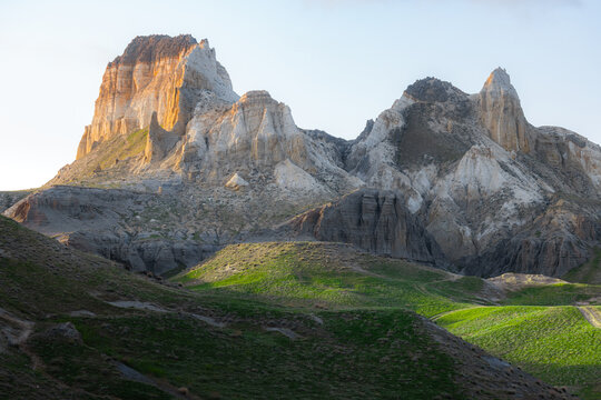 View of the striking limestone formations of Airakty mountains rising above vibrant green grassy slopes under the warm glow of the golden hour in Shetpe, Mangystau Region, Kazakhstan.