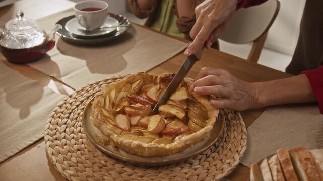 Senior Caucasian woman slicing baked apple tart with knife on dining table during family tea time, top view. Footage suitable for Thanksgiving ads, senior lifestyle and bakery promotions