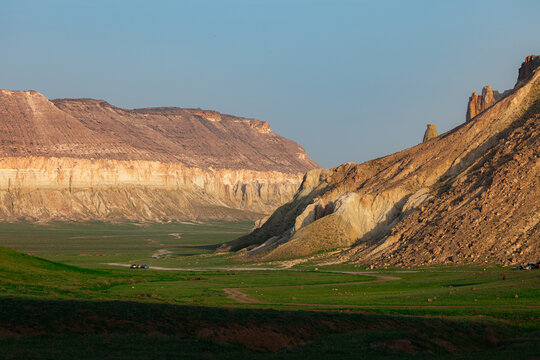 View of the rocky cliffs of Airakty rising above a green valley with a dirt road in the desert landscape of Shetpe, Mangystau Region, Kazakhstan.