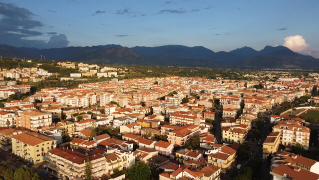 Aerial cityscape of Scalea town in Calabria, Italy, illuminated by warm sunlight with dark dramatic mountains in the background.