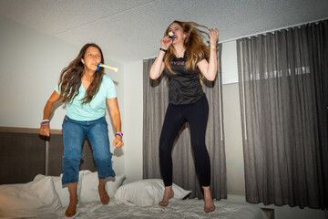 Naklejka premium Women Jumping on Bed During Indoor Celebration With Party Blowers