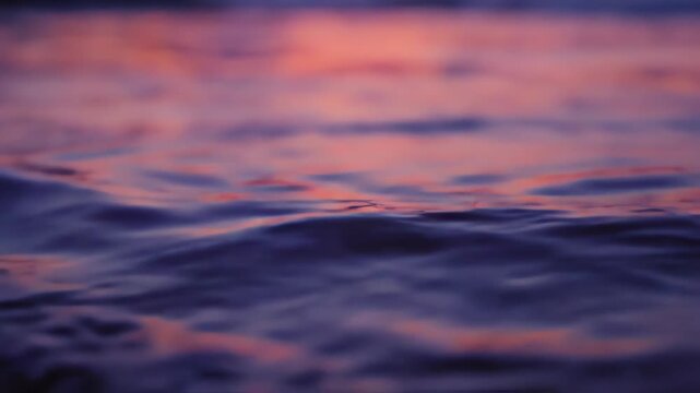 Abstract water ripples on a calm surface reflecting the fading light of dusk with a slow macro dolly shot showing intricate liquid textures