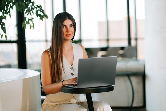 Professional woman with long brown hair working on a laptop in a bright modern office workspace