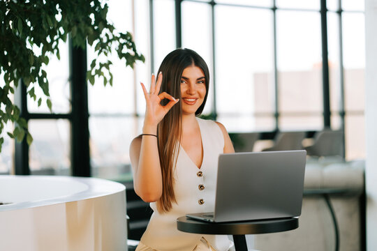 Woman gesturing while working on a laptop in a modern office