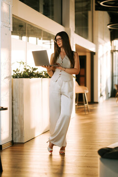 Professional woman working on a laptop while standing in a bright modern office during the afternoon
