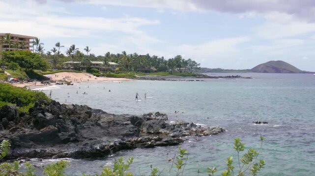 Wailea-Makena coastal area of Maui, Hawaii with a volcanic rock shoreline, tourists on the white sand Polo beach beyond and the Puu Olai Cinder Cone in the distance. Wailea Beach Path.
