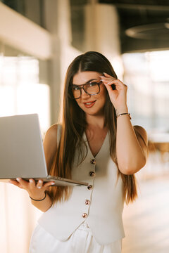 Woman with glasses holding a laptop in a bright office