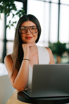 Professional woman smiling while sitting at a table with her laptop in a modern bright office space