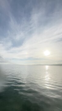 Vertical seascape with sun halo phenomenon over calm ocean and streaked clouds, 4K