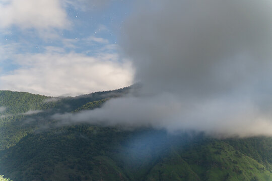 View of the lush green mountains along the Ali Bedni Bugyal trek shrouded in thick clouds under a soft sky in Chamoli, Uttarakhand, India.