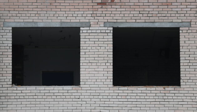 Two square window openings without window frames in a wall made of white brick