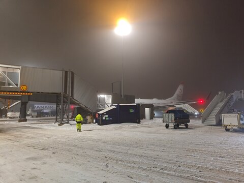 Rovaniemi, Finland-Dec.3rd 2025: snow-covered tarmac at Rovaniemi Airport at night, featuring jet bridge, parked airplane, and ground crew