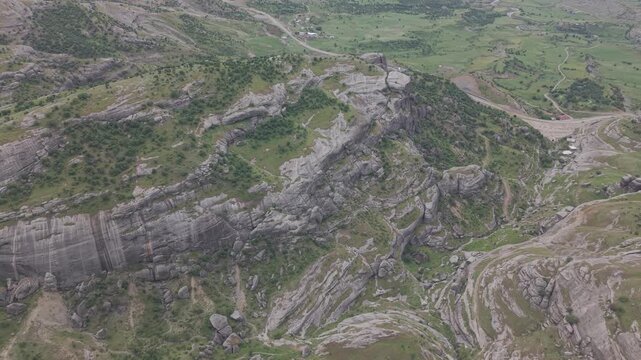Smooth 4K 30fps aerial flight from above with a gentle rightward movement, revealing massive rock formations and a vast green valley. Flat color profile, ideal for color grading and LUTs.