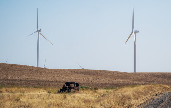 View of an abandoned rusted vintage car in a dry grassy field with wind turbines in the background in Oregon, United States.