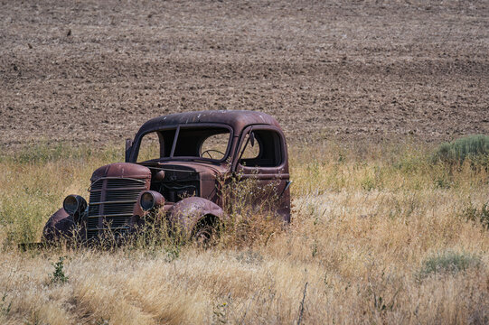 View of an abandoned rusted vintage car sitting in a dry grassy field with a plowed field in the background in Eastern Oregon, Oregon, United States.