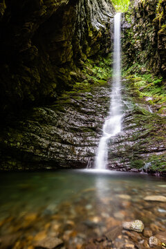 View of a cascading waterfall flowing over mossy rock walls into a clear pool in Zeri, Tuscany, Italy.