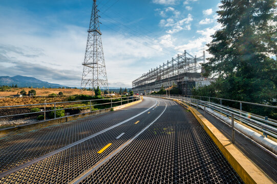 View of Bonneville Dam featuring a metal grate bridge, power lines, and surrounding landscape in Cascade Locks, Oregon, United States.