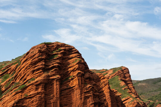 View of the iconic red sandstone rock formations of Jety-Oguz featuring rugged cliffs and patches of green vegetation under a bright blue sky in Jety-Oguz, Issyk-Kul Region, Kyrgyzstan.