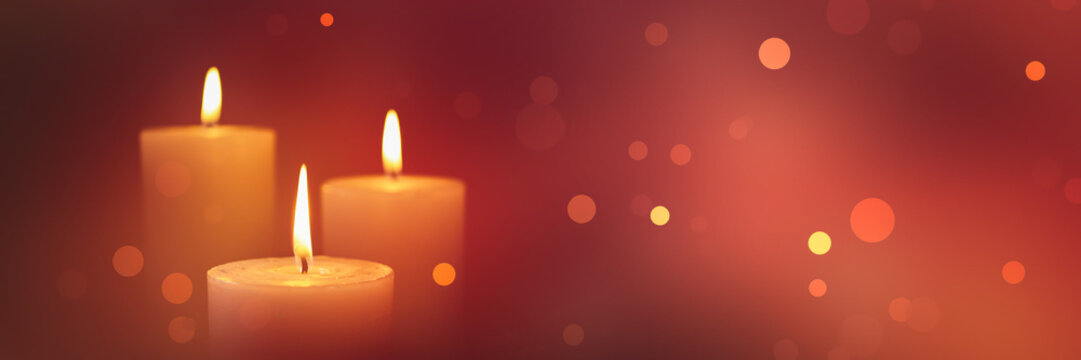 three burning candles isolated on blurred red background banner with bright defocused lights, festive concept with copy space for christmas and december holiday season