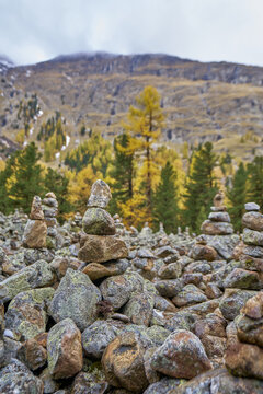 View of stone cairns in the Engadin valley surrounded by autumn larch trees and mountain slopes in Grisons, Switzerland.