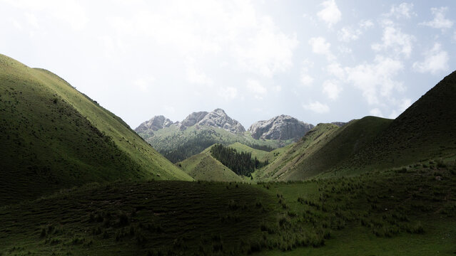 View of Teskey-Torpu mountain range with lush green grassy slopes, rocky peaks, and a cloudy sky in Naryn District, Naryn Region, Kyrgyzstan.