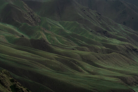 View of Teskey-Torpu mountain range with rolling green slopes and shadows under a soft light in Naryn District, Naryn Region, Kyrgyzstan.