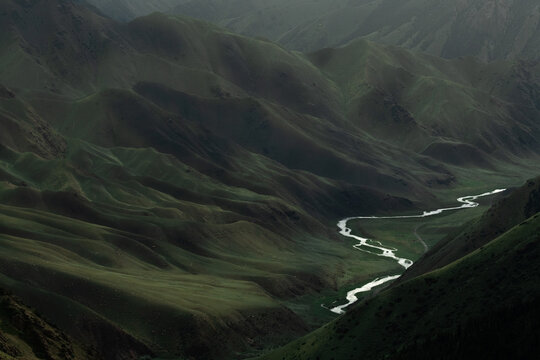 View of the Teskey-Torpu mountain range with a winding river flowing through the lush green valley in Naryn District, Naryn Region, Kyrgyzstan.