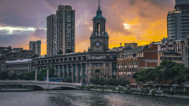 View of the historic Shanghai Postal Museum with its iconic clock tower, situated along the Suzhou Creek with a bridge in the foreground under a dramatic sunset sky in Shanghai, Shanghai, China.