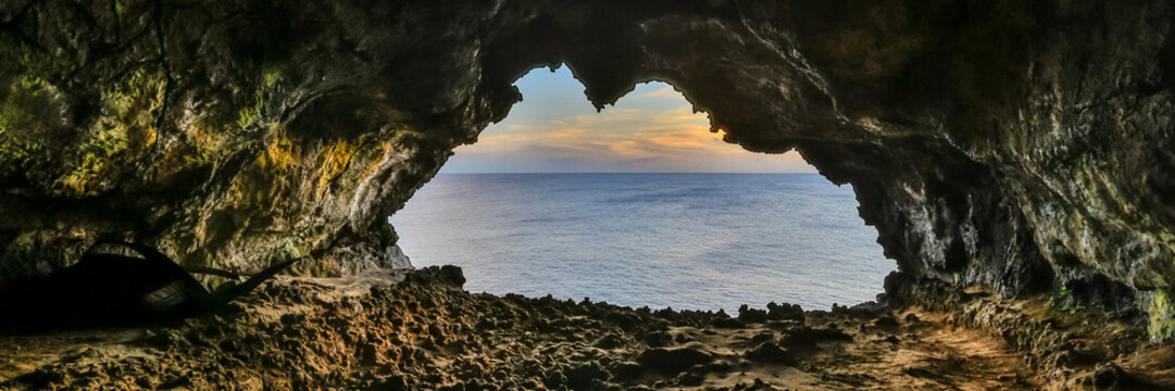 View of a sea cave opening looking out over the calm ocean at sunset with rugged rock formations and a soft sky in Easter Island, Valparaiso, Chile.