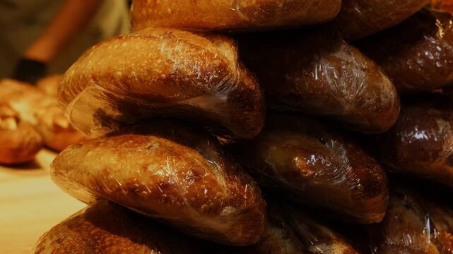 Handmade bread loaves packaged with plastic foil stack on table closeup. Bakery shop fresh products prepared to sell and delivery in storage