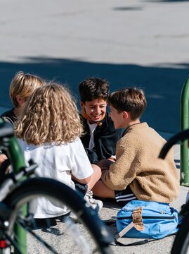 Sikh boy laughing with friends by a green bike rack, featuring weathered textures and low sun light for school life and inclusion campaigns, with copy space