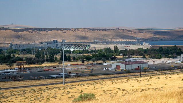 View of McNary Lock and Dam with industrial structures and dry grassy hills in the background in Umatilla, Oregon, United States.