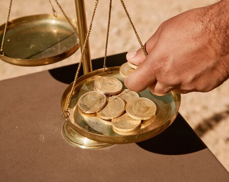 Gold coins being weighed on a brass beam balance by a person, featuring glowing metallic textures and a dark surface for investment and wealth themes