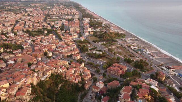 Scenic aerial panoramic sweep over the historic town of Scalea, featuring terracotta roofs, beautiful Mediterranean coastline and mountains at twilight, Italy, 1080p.