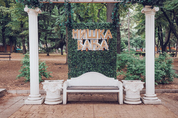 Obraz premium July 12, 2026, Niska Banja, Serbia: Decorative park bench and ivy sign installation at famous spa resort.