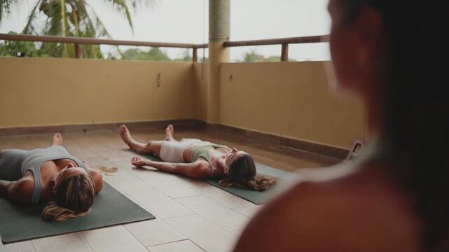 Two women relaxing in corpse pose at the end of a yoga class on a tropical balcony latina yoga instructor in mexico
