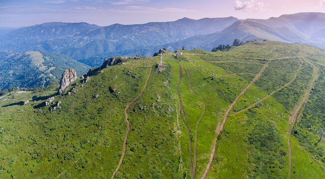 Ski lift lines and dirt tracks crossing green mountain ridge with rock outcrops, layered peaks behind. Travel concept - Babin Zub in Stara Planina park, Serbia