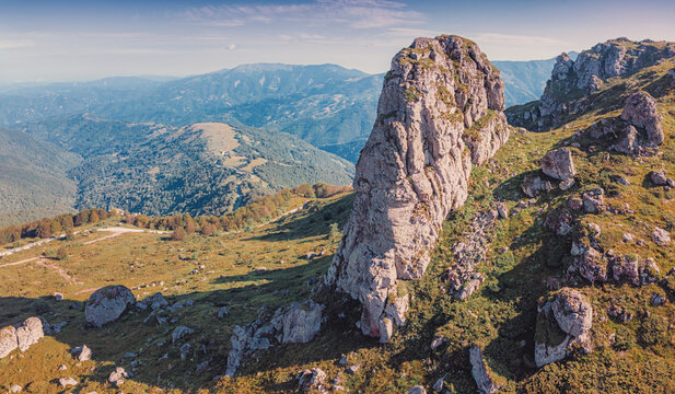 Green alpine meadow with dramatic limestone rock formation Babin Zub rising above layered mountain valleys at summer sunrise. Scenic nature background - Stara Planina park in Serbia, Balkans.