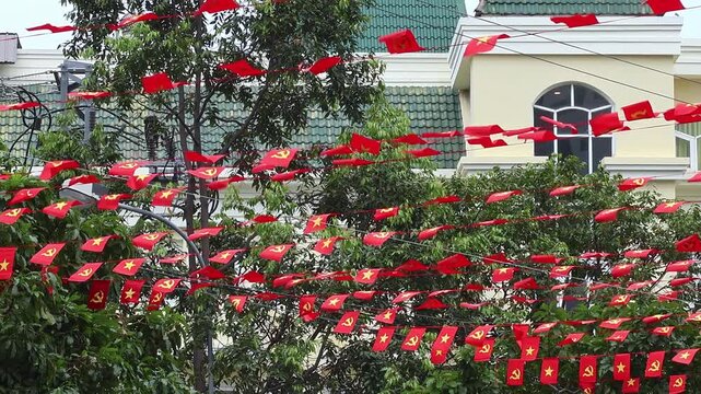 Vietnamese National Flags Flying on City Street for Independence Day. Red flags flutter above homes and trees. National holiday, public decoration and civic pride concept.