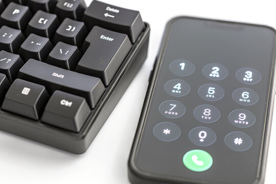 Detailed close-up of a black mechanical keyboard featuring the Enter key, positioned next to a smartphone displaying a dial pad with numbers and a glowing green call button ready to connect