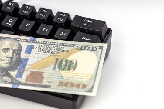 Close-up shot of a hundred dollar bill marked movie prop use only lying across a black mechanical keyboard near the enter and delete keys, symbolizing online money concepts