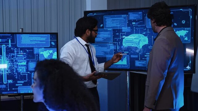 Male tech developer pointing at automotive design wireframe on large screen display while presenting software system architecture to colleague during corporate office project review
