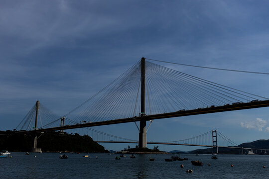Suspension bridge spans across water with boats below under a clear sky