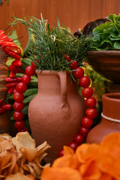 terracotta jar with rosemary sprigs and cherry tomato garland next to red pimenta dedo de mo&ccedil;a and crisps for brazilian feijoada buffet, catering close up vertical shot