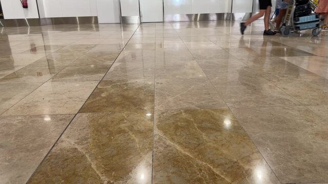 Anonymous people's legs walking through a busy terminal hall. Low-angle view of passengers with wheeled bags on a reflective marble floor