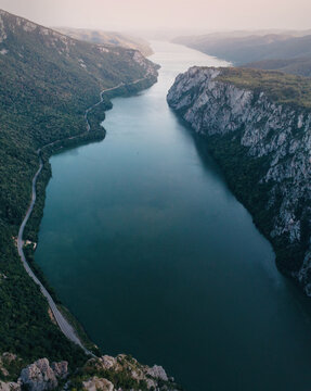 Danube River winding between towering cliffs and lush mountains in the Iron Gates gorge, with a road following the riverbank