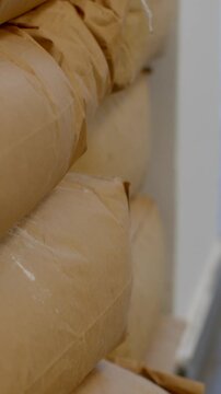 warm bakery interior with stacked baguettes wrapped in crinkled brown paper, tied with string on pale shelf, bread texture, soft light, cozy storage vertical, with