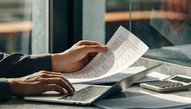 Tax professional reviewing financial documents with a calculator and laptop at an office desk, representing accounting, tax preparation, financial planning, business finance, and professional document